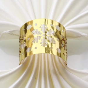 Detail of a gold snowflake napkin ring with a hollow design on a white cloth