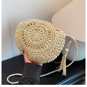 Dettaglio della borsa a tracolla rotonda in paglia con texture all'uncinetto e nappe di legno