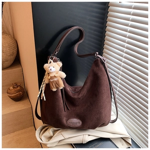 Detail of a brown suede hobo tote bag featuring a cute bear pendant and a fine leather strap