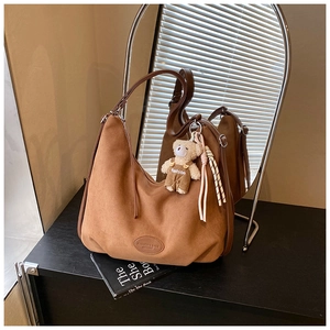 Close-up of brown suede tote bag featuring a cute bear charm and embossed logo detail