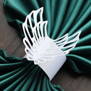 Macro detail of laser-cut white paper napkin ring with elegant wing design on green fabric