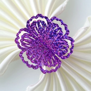 Close-up of laser-cut purple glitter flower napkin ring on white satin fabric