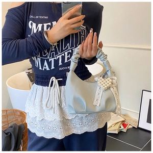 Detail of light blue crescent bag with lace bow and pearl heart charm on a textured surface
