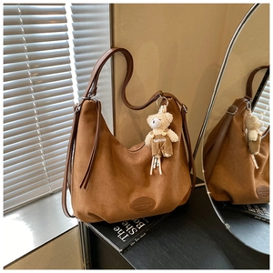 Detail of dark brown matte leather tote bag with logo patch and cute plush bear charm