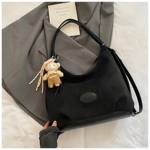 Detail of black suede hobo bag with teddy bear charm on grey suit background