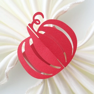 Detail of laser-cut red pumpkin paper napkin ring on a white folded cloth