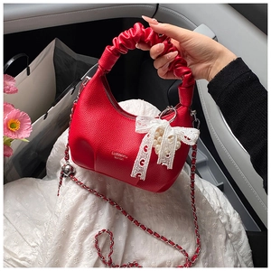 Macro detail of red crescent underarm bag with lychee texture and lace bow decor
