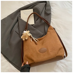 Detail of brown suede tote bag with logo badge and cute teddy bear keychain charm