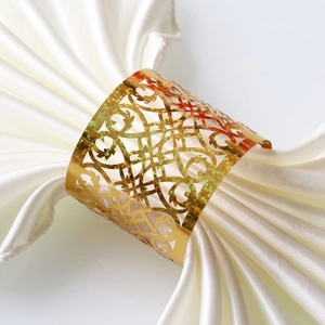 Sparkling gold hollow pattern napkin ring on white silk cloth for elegant table decor