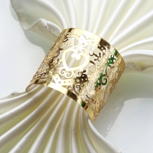 Close-up of golden hollow heart napkin ring with intricate vine pattern on silk