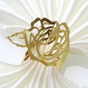 Close-up of golden hollow rose napkin ring on white silk fabric for wedding decor