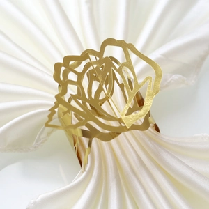 Detailed view of a golden hollow rose napkin ring on a white satin fabric background