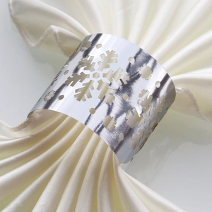 Macro detail of silver mirror snowflake napkin ring on white satin fabric for festive tables