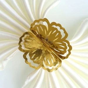 Macro detail of laser-cut golden flower napkin ring on elegant white satin fabric