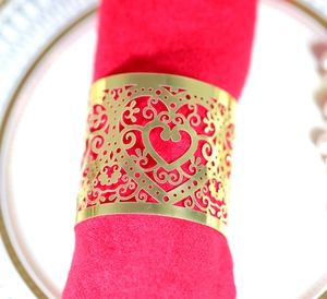 Close-up of gold laser-cut heart napkin ring on red cloth over a white ceramic plate