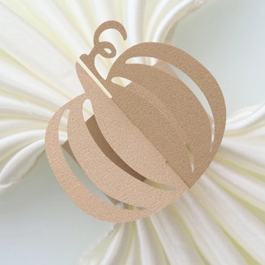 Detail view of laser-cut bronze pumpkin paper napkin ring on a white cloth background