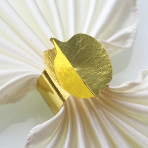Detailed close-up of a golden leaf-shaped napkin ring on a folded white cloth