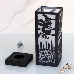Black paper Halloween lantern with witch and pumpkin cutouts on a marble base