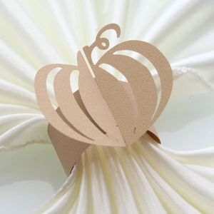 Detail showing laser-cut pumpkin paper napkin ring on elegant beige satin fabric