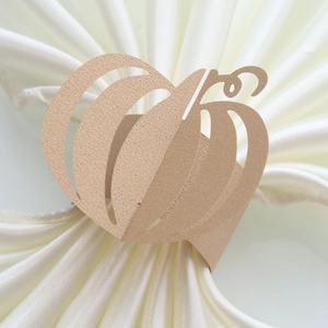 Detail of laser-cut champagne gold pumpkin paper napkin ring on white satin fabric