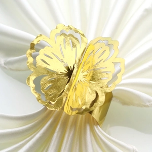Detail of a hollow flower napkin ring in gold metal finish on a white silk cloth