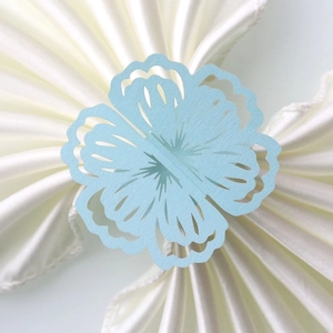 Macro view of laser-cut light blue floral paper napkin rings on a white satin cloth