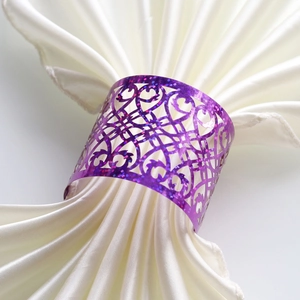 Detailed view of purple glitter napkin ring with laser-cut baroque pattern on white satin