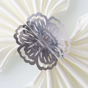 Detail of silver hollowed flower napkin ring with laser-cut petals on white fabric