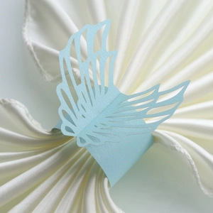 Macro shot of laser-cut light blue pearlescent paper napkin ring in angel wing design