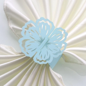 Macro view of light blue laser-cut flower napkin ring on a white satin cloth