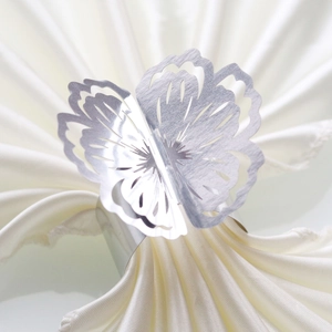 Detailed close-up of a silver hollow butterfly napkin ring on a white silk cloth