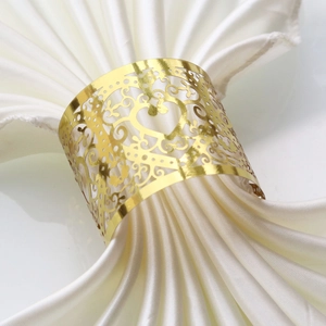 Macro shot of gold hollow heart napkin ring with laser-cut floral patterns on white silk