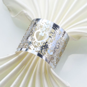 Detail of silver hollow heart napkin ring with laser-cut patterns on satin fabric