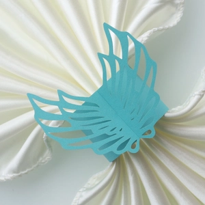 Detailed macro view of laser-cut turquoise wing-shaped napkin ring on white satin fabric