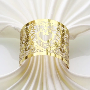Close-up of golden hollow heart napkin ring with laser-cut floral patterns on white silk