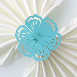 Macro shot of sky blue laser-cut paper napkin ring with hollow floral pattern on white satin