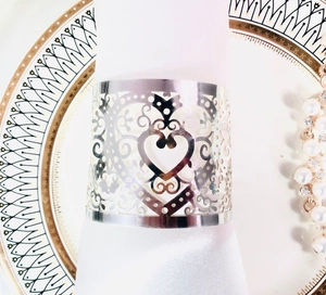 Silver laser-cut heart napkin ring with elegant scroll patterns on a white silk napkin