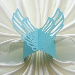 Macro detail of laser-cut light blue angel wing napkin ring on white satin fabric background