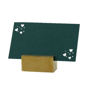 Golden metal place card holder with a dark green heart pattern card for weddings