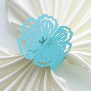 Detailed top view of light blue laser-cut flower paper napkin ring on white satin fabric