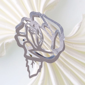 Detailed view of silver rose napkin ring with intricate hollow metal design on white cloth