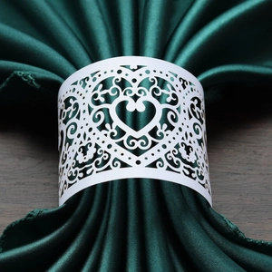 Detail of white laser-cut heart napkin ring on dark green satin fabric over wood table