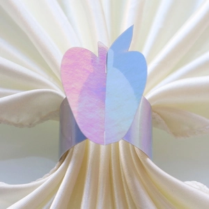 Close-up of apple-shaped napkin ring with iridescent purple laser finish on white satin