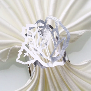 Detail of silver rose cutout napkin ring on white silk fabric with mirror finish