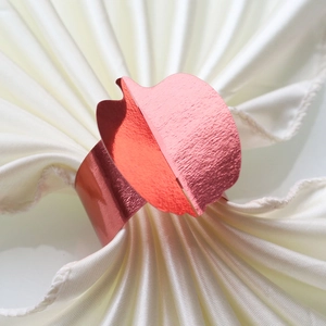 Detail of red metallic leaf napkin ring on white satin fabric for festive table decor