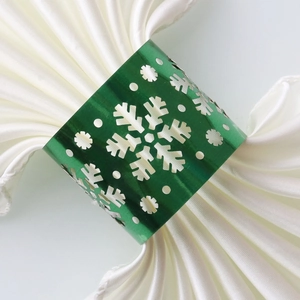 Detailed close-up of metallic green snowflake napkin ring with laser-cut design on white fabric