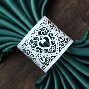 Elegant white laser-cut heart napkin ring with vine patterns on a dark satin cloth