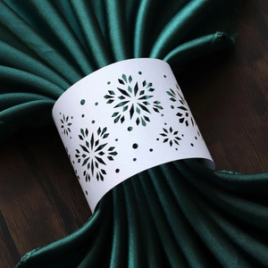 Elegant white laser-cut snowflake paper napkin ring on a dark green silk napkin