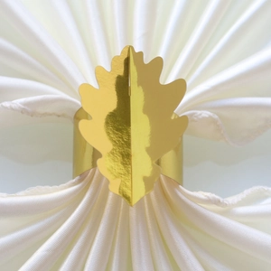 Détail d'un rond de serviette doré en forme de feuille sur une serviette en soie blanche