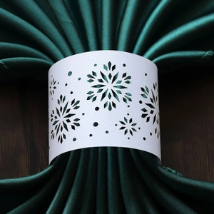 Close-up of white laser-cut snowflake napkin ring on green satin for Christmas decor